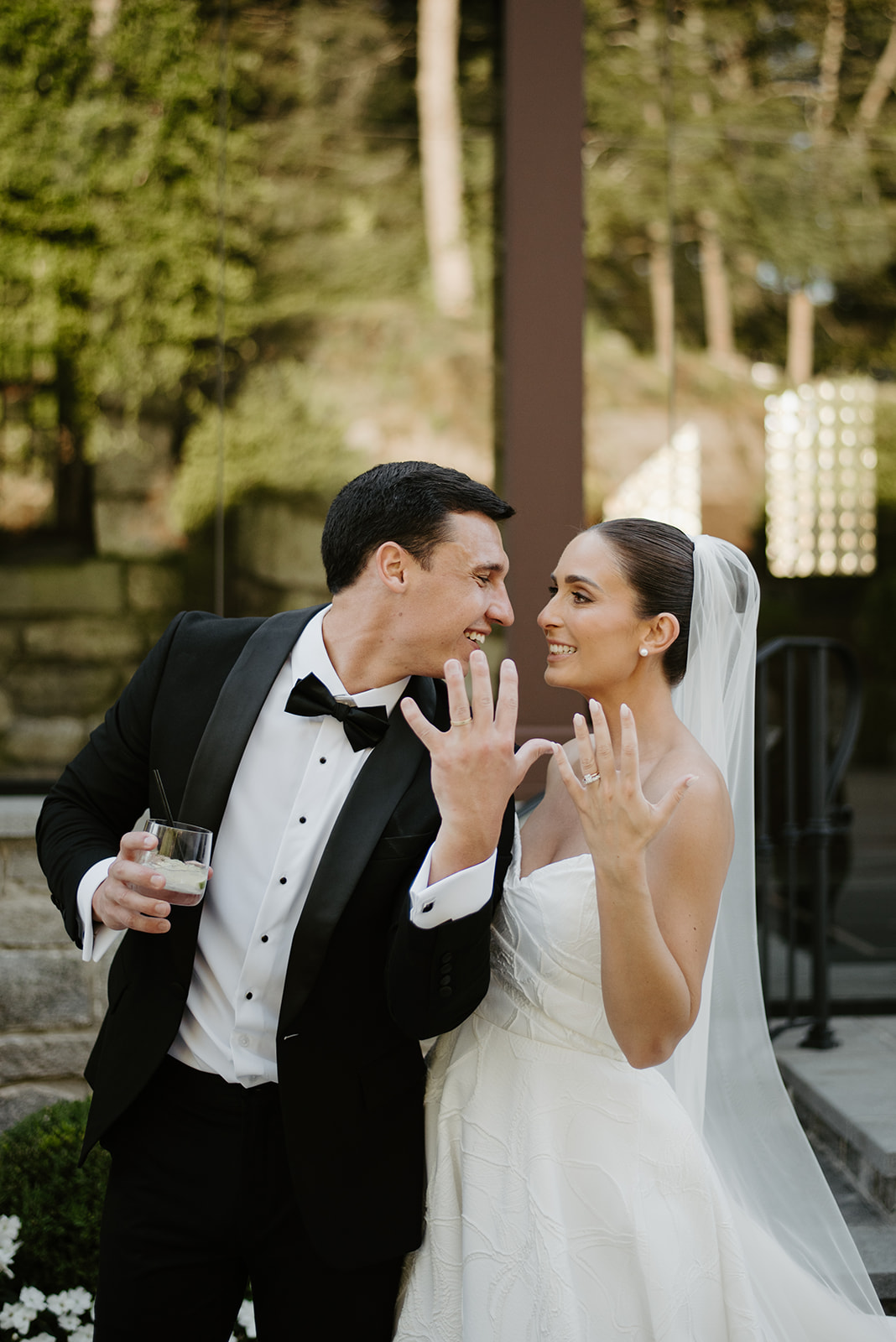 Joyful newlyweds showing off their new wedding rings and laughing together during cocktail hour.